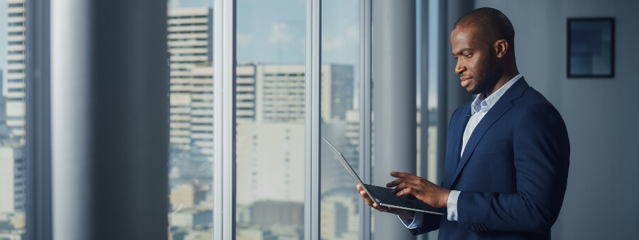 como investir: homem usando computador em frente à janela de prédio corporativo