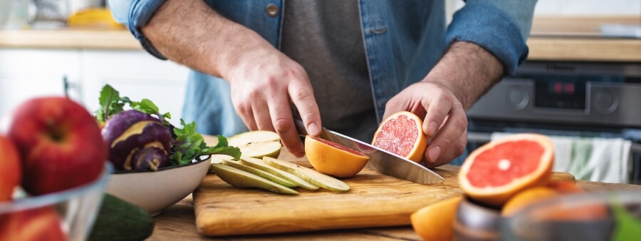Dia da Saúde e Nutrição: imagem de mãos masculinas cortando frutas
