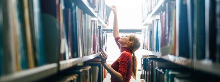 Dia do Bibliotecário: bibliotecária guardando livro em prateleira