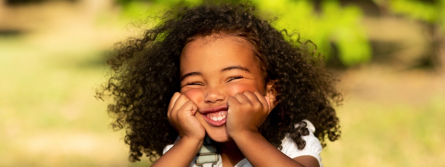 Crianças felizes: menina sorrindo com mãos junto ao rosto