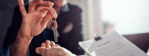 Como fazer um contrato de aluguel: pessoa entregando chaves e contrato para outra